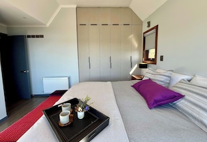 Ein modernes Schlafzimmer mit Bett, Nachttisch, Kommode und einem Fenster mit Blick.