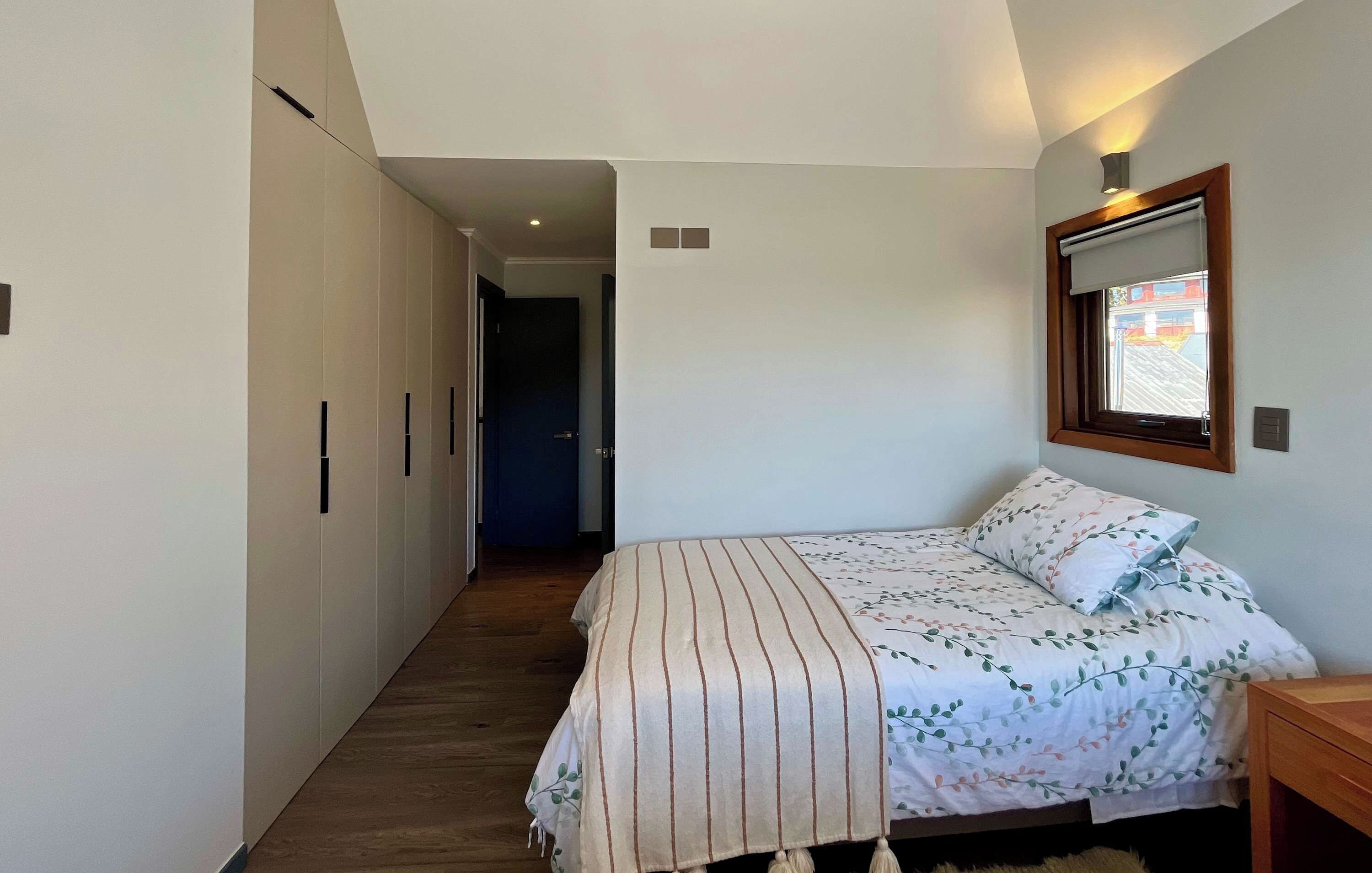 A bedroom with a bed, a nightstand, a wardrobe, and a window.