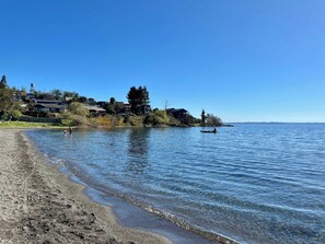 Una playa con agua cristalina, una orilla arenosa y casas al fondo.