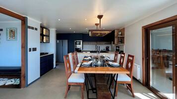 A modern kitchen with built-in appliances, a dining area with a wooden table and chairs, and a glass door leading to an outdoor area.