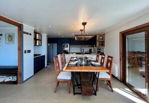 A modern kitchen with built-in appliances, a dining area with a wooden table and chairs, and a glass door leading to an outdoor area.