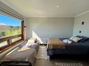 A bedroom with two beds, a view of a mountain, and a window.