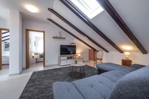 A modern loft bedroom with a skylight, a large window, a television, and a cozy seating area. - Villa Pizzelli (Dubrovnik)