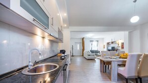 A modern kitchen with a stainless steel sink, a built-in oven, and a dining area with a wooden table and chairs. - Villa Pizzelli (Dubrovnik)