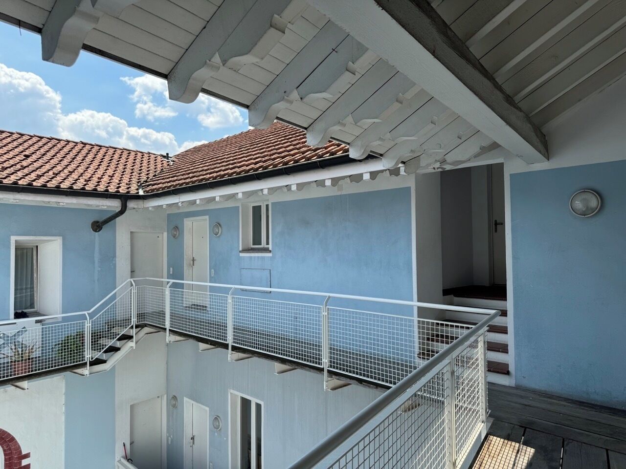 Un immeuble à plusieurs étages doté d’un balcon, d’un toit en tuiles et d’une façade bleue.