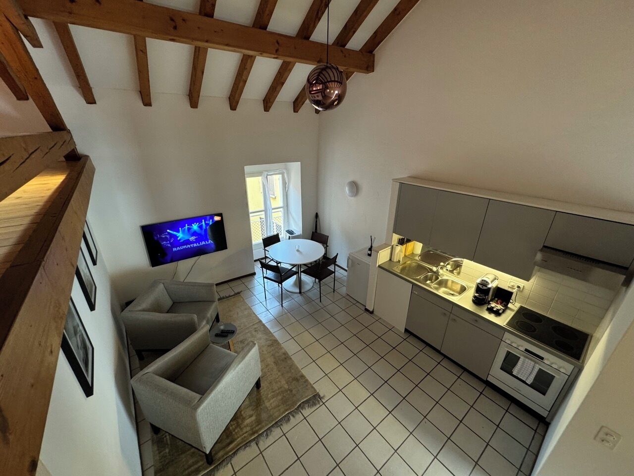 A compact kitchen with a dining area, a TV mounted on the wall, and a wooden ceiling.