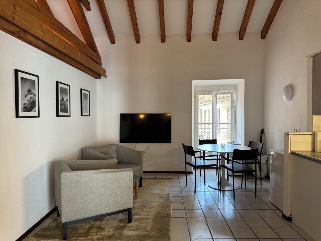 A living room with a sofa, a TV, and framed pictures on the wall. There is a dining area with a table and chairs.