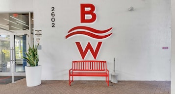 Entrada de um edifício com um banco vermelho, uma planta em vaso e um painel de sinalização de alarme de incêndio.