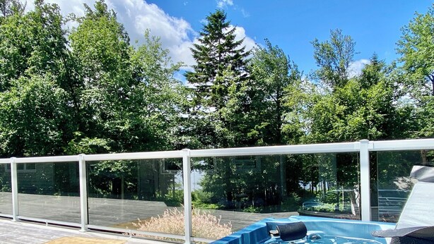 Un jacuzzi en una terraza de madera con barandillas de vidrio, rodeado de árboles.