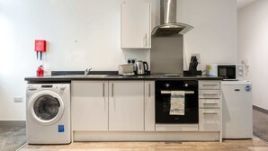 A compact kitchen with a washing machine, oven, microwave, and a fire extinguisher.