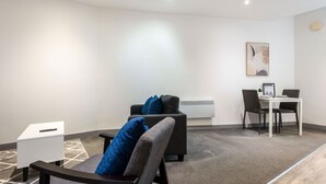 A modern room with a grey sofa, a small white table, and a dining table with chairs.