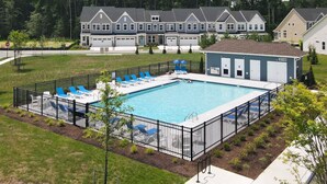 A rectangular swimming pool with blue lounge chairs and a fenced deck area.