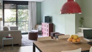 Een moderne woonkamer met een eethoek, een bank, een televisie en een groot raam.