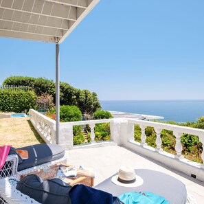Een balkon met uitzicht op zee, witte leuningen en tuinmeubilair.