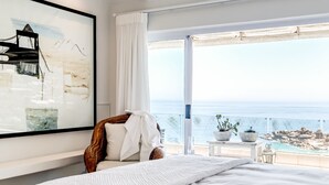 A bedroom with a large bed, a view of the sea, and a painting on the wall.