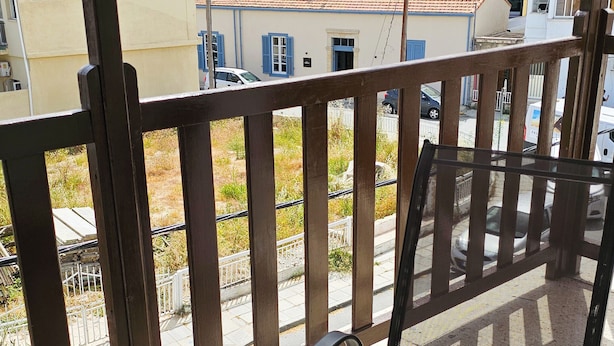 Un balcon doté d’une table et de chaises en verre, offrant une vue sur un bâtiment d’hôtel avec de nombreux balcons et un toit recouvert de tuiles rouges.