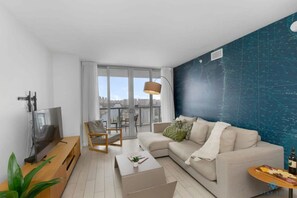 Uma sala de estar moderna com sofá, mesa de centro, TV e uma grande janela com vista para a cidade.