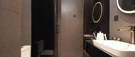 Un baño moderno con cabina de ducha de vidrio, un lavabo blanco y un espejo con marco dorado.