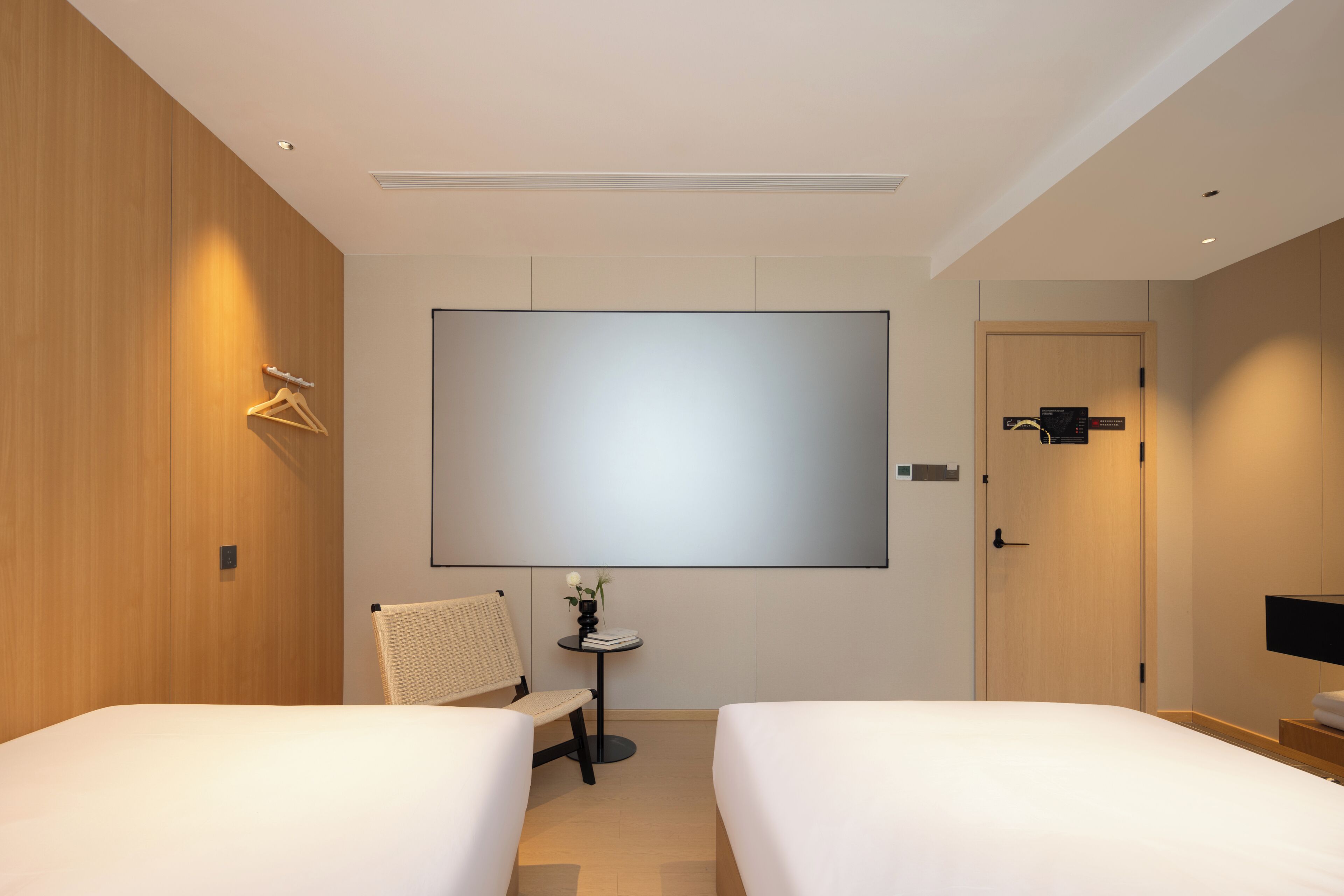 A hotel room with two beds, a flat-screen TV, a small table with a vase, and a chair.