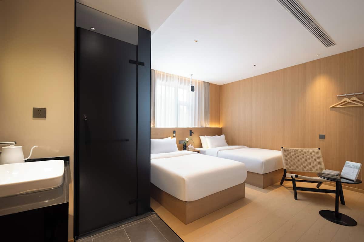 Ein Hotelzimmer mit zwei Betten, einem Schreibtisch, einem Stuhl, einem Waschbecken und einem Spiegel.