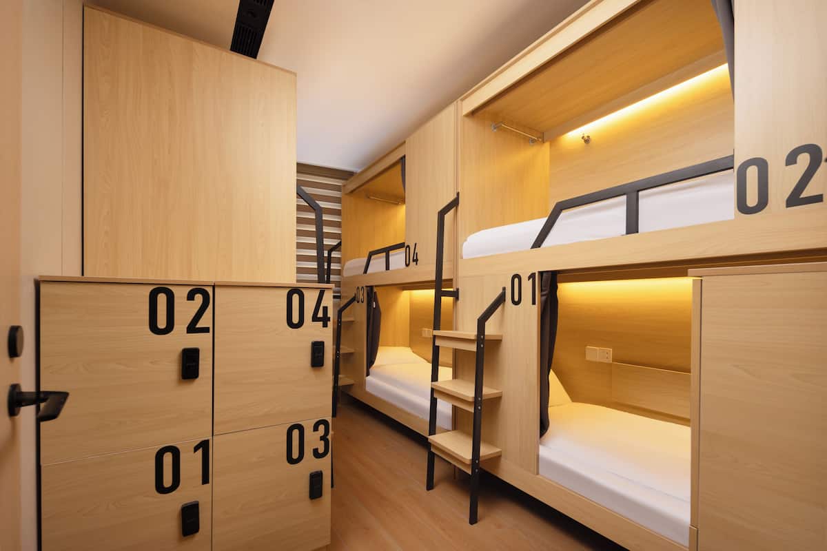 Ein modernes, kompaktes Hotelzimmer mit Stockbetten, Holzschränken und einer Treppe.