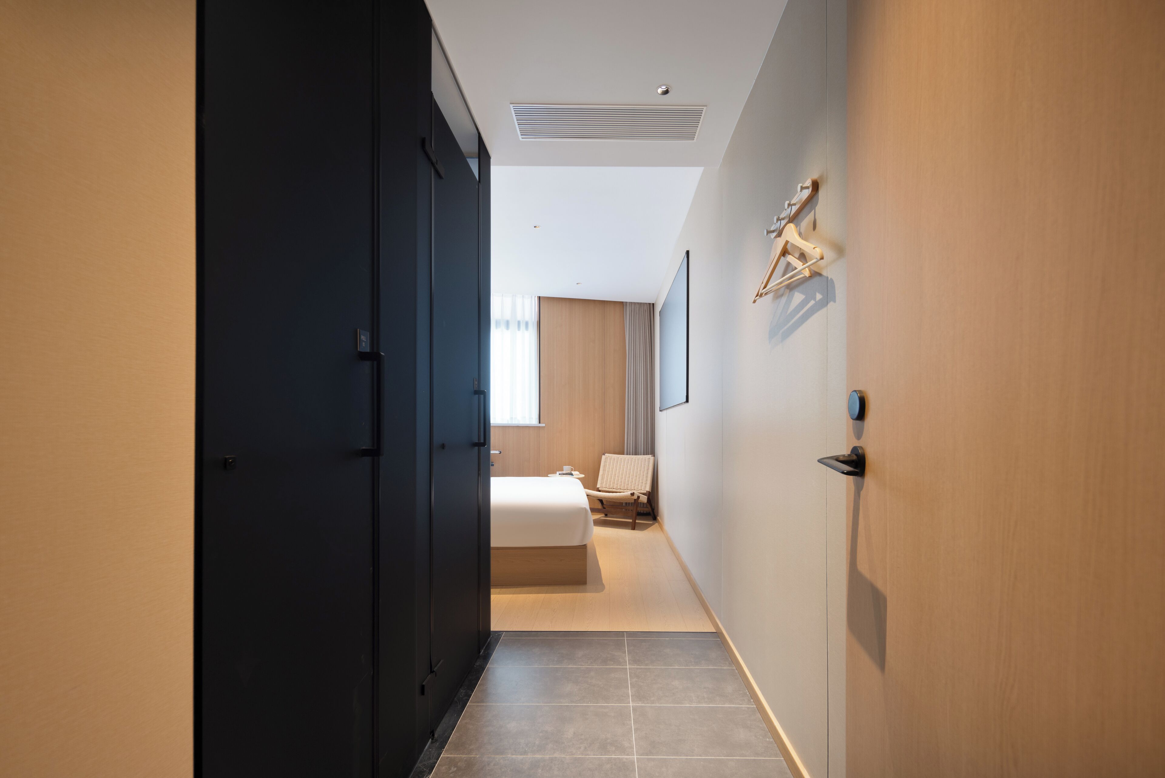 A modern hotel room with a large bed, a chair, and a wardrobe.