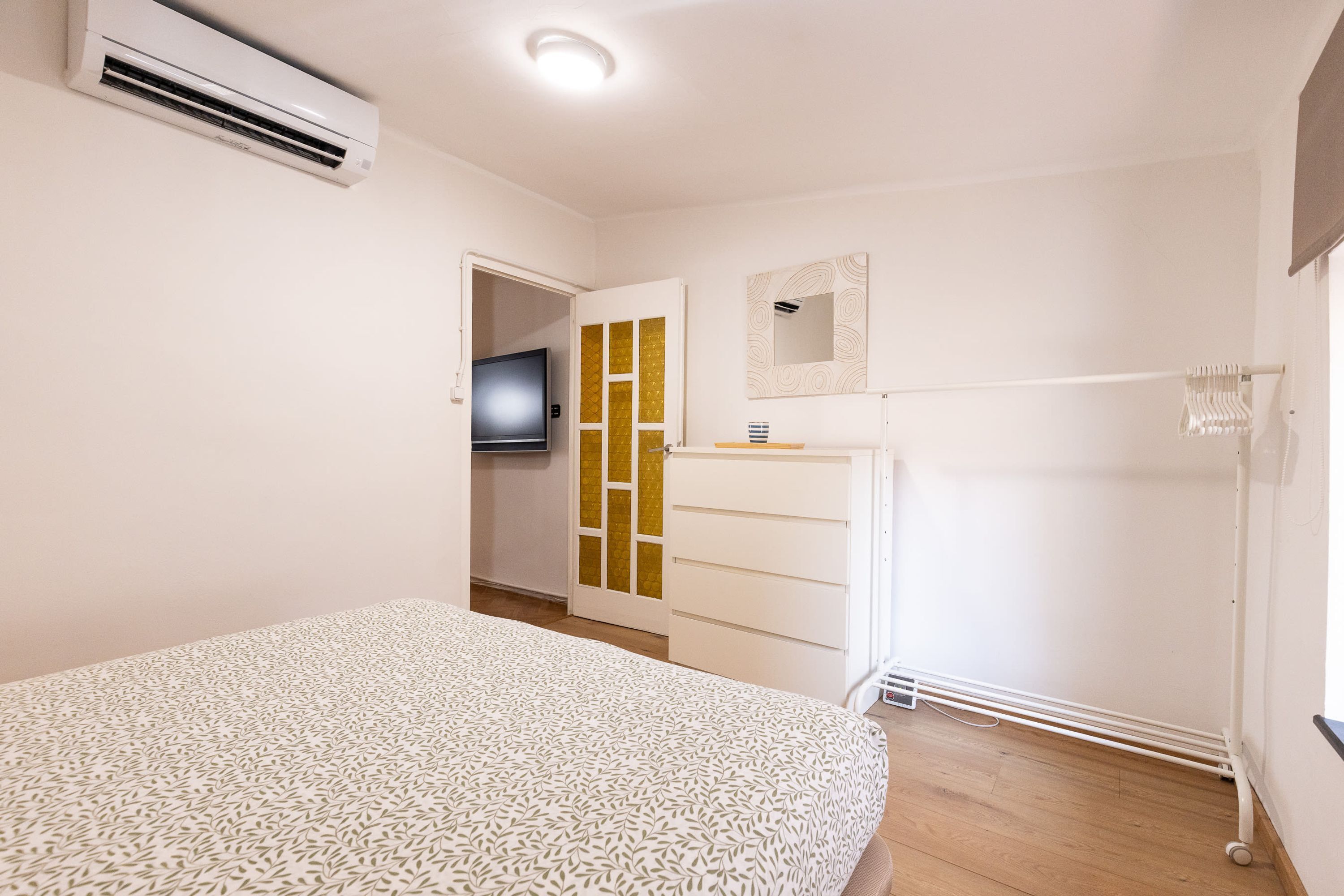 A bedroom with a bed, a wardrobe, a television, and an air conditioning unit.
