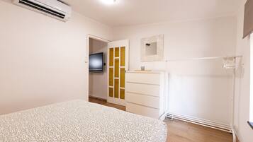 A bedroom with a bed, a wardrobe, a television, and an air conditioning unit.