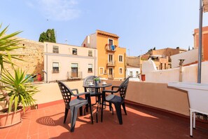 A rooftop terrace with a table and chairs, a potted plant, and a view of surrounding buildings. - Unik Vacation Sant Joan (Tarragona)