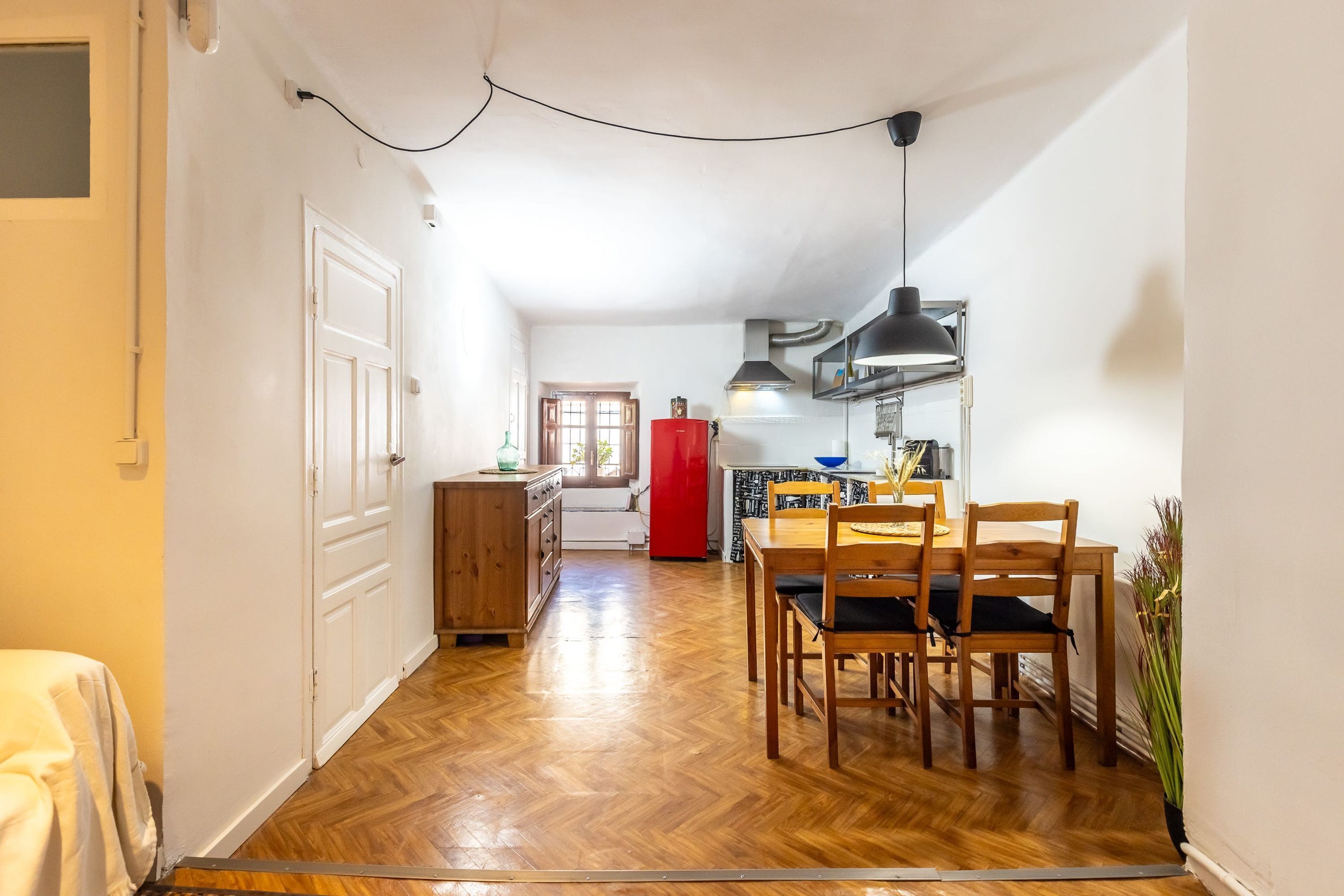 Une cuisine compacte avec un coin repas, un plancher en bois et un réfrigérateur rouge.