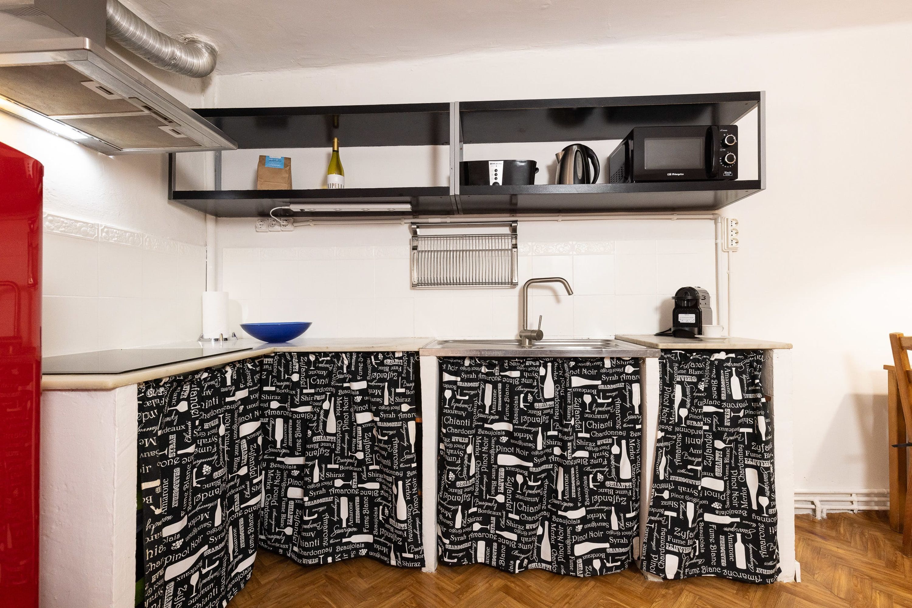 Cocina compacta con un lavamanos, microondas y hervidor sobre una estantería.