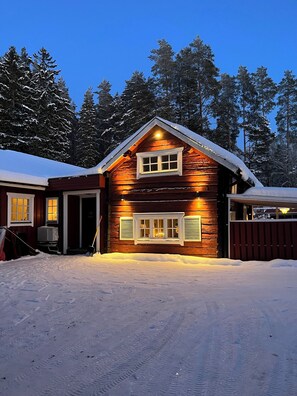 A log cabin with a snow-covered roof, a front porch, and a garage.