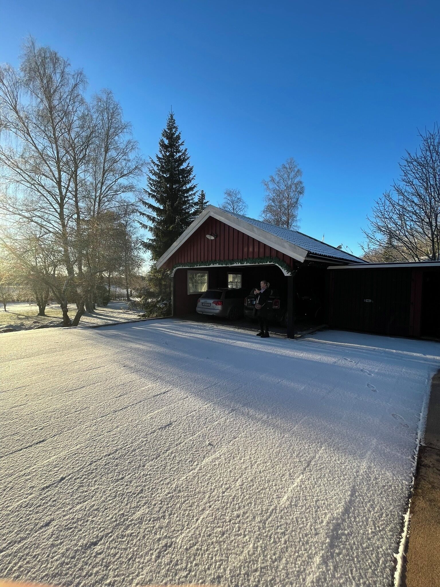 A red barn with a covered porch, snow on the ground, and trees in the background.