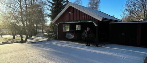 A red barn with a covered porch, snow on the ground, and trees in the background.