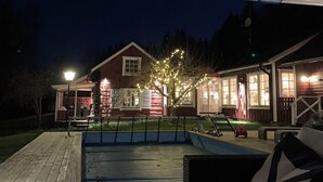 A covered outdoor area with a pool, a wooden deck, and a house with string lights. - Charming Property With Private Pool (Marsta)