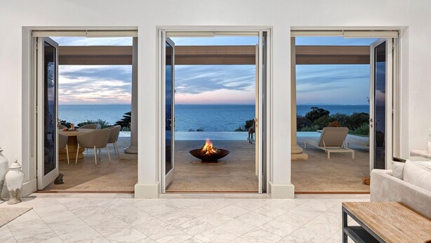 A modern living room with a large glass door leading to a patio with a fire pit and outdoor seating. - The Bay Crest Manor Views Pool Beach (Mount Eliza)