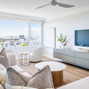 A modern living room with a city view, a ceiling fan, a flat-screen TV, and a minimalist design. - Charming Central Apartment Aquene bay (Cape Town)