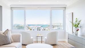 A modern living room with a large window, a sofa, two armchairs, a coffee table, and a sideboard. - Charming Central Apartment Aquene bay (Cape Town)