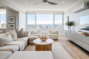 A modern living room with a sofa, armchairs, a coffee table, and a view of the city through large windows. - Charming Central Apartment Aquene bay (Cape Town)