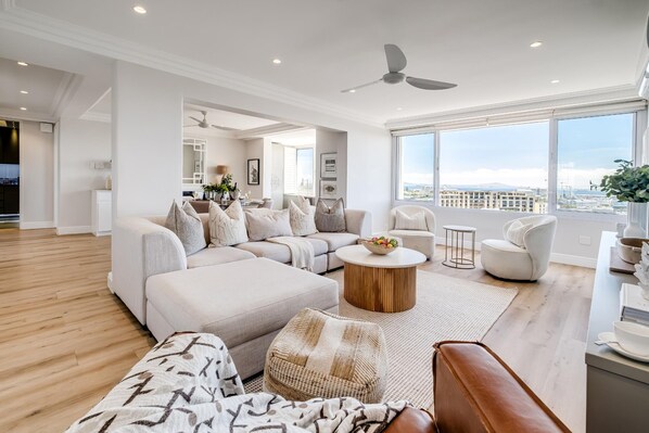 A spacious living room with a large sectional sofa, a round coffee table, and a view of the city through large windows. - Charming Central Apartment Aquene bay (Cape Town)