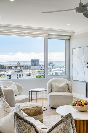 A modern living room with a city view, a ceiling fan, and a bowl of fruit on the table. - Charming Central Apartment Aquene bay (Cape Town)