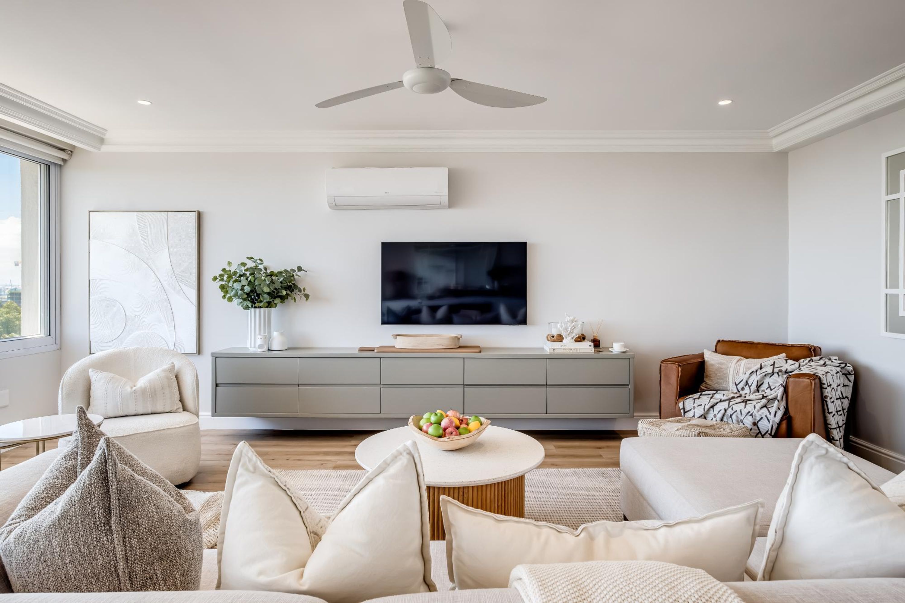 A modern living room with a sofa, a coffee table, a TV, and a ceiling fan.