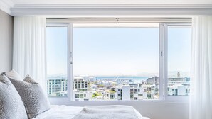 A bedroom with a large window, a bed with white linens, and a view of a cityscape. - Charming Central Apartment Aquene bay (Cape Town)