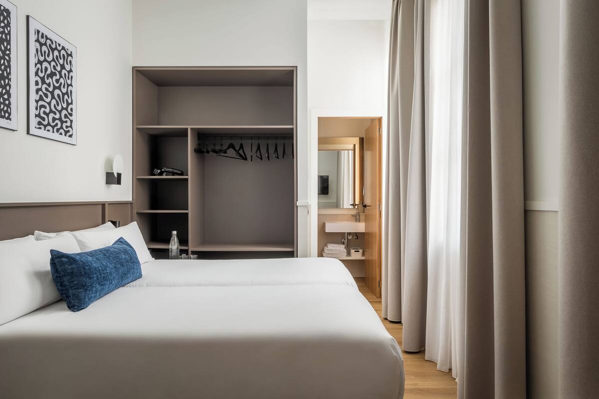 A hotel room with a large bed, a wardrobe, and a bathroom visible through an open door.