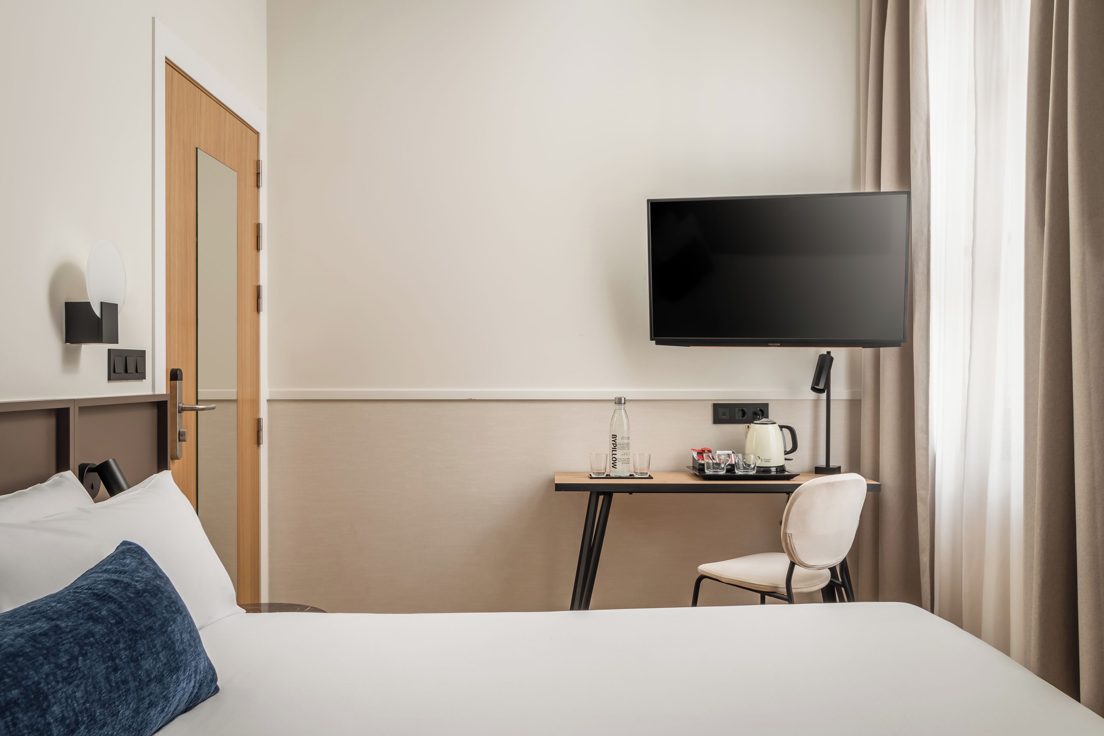 Ett hotellrum med en säng, ett skrivbord med en stol, en tv och en spegel.
