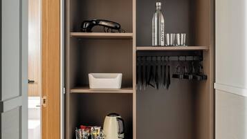 Una cocina compacta con un refrigerador empotrado, cafetera y hervidor sobre la encimera.