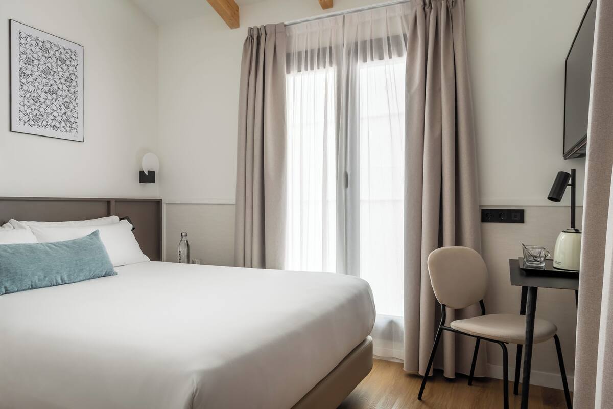 A hotel room with a large bed, a desk with a chair, a water bottle, and a framed picture on the wall.