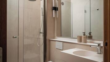 Un baño moderno con cabina de ducha de vidrio, un lavabo blanco y un espejo grande.