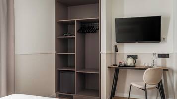 A hotel room with a wardrobe, a desk with a chair, a flat-screen TV, and a small refrigerator.