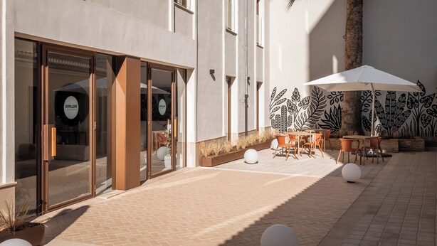 A modern building with large glass doors, outdoor seating with umbrellas, and decorative wall art. - BYPILLOW Sinfonía  (Valencia)